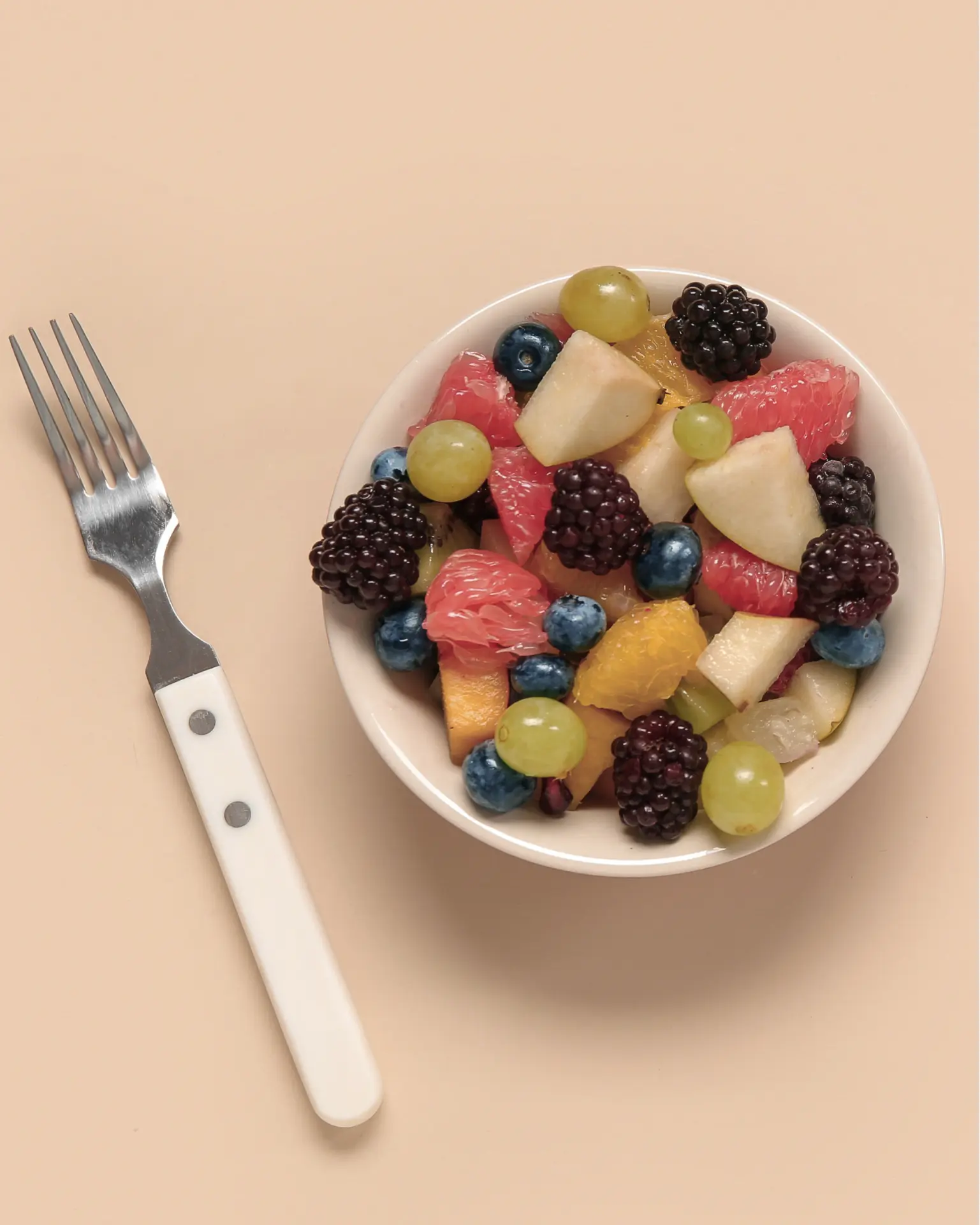 A bowl of mixed fruit with berries, grapes and citrus, seen from above